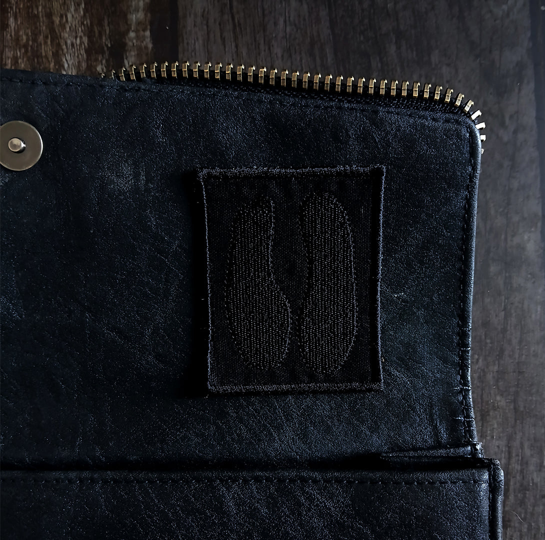 Close-up of a black purse with a cloven hoof patch on a dark background