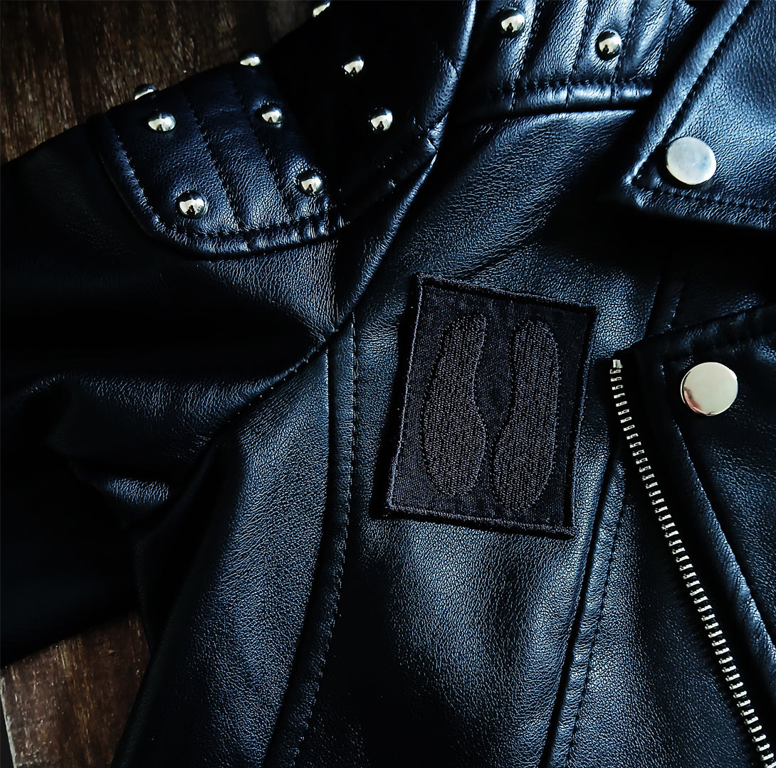 Close-up of a black leather jacket with studs and a patch of a cloven hoof on a wooden surface