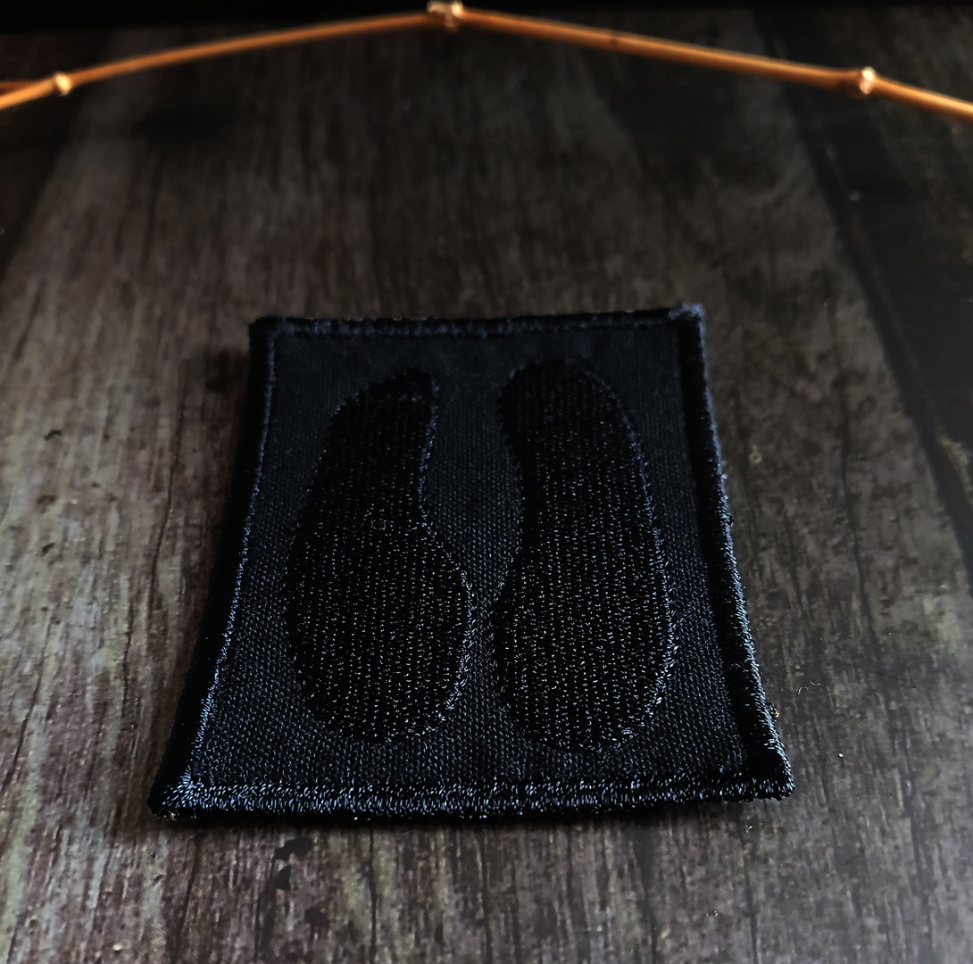 Black embroidered patch with a cloven hoof design on a wooden surface