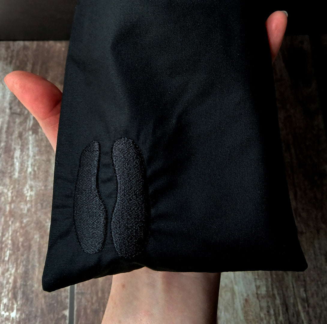 Black tarot card bag with cloven hoof embroidery held by a hand on a wooden surface