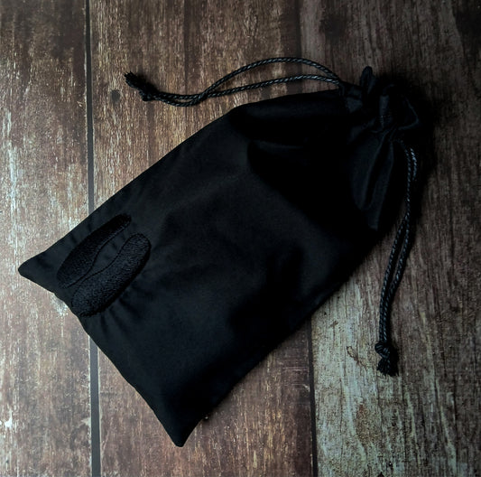 Black drawstring tarot pouch with cloven mark embroidery on a wooden surface